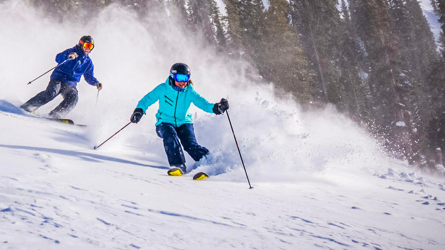 Two happy skiers in turning in soft snow with snow flying in the air